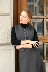a lady in a black knit top, a grey vest and a grey skirt